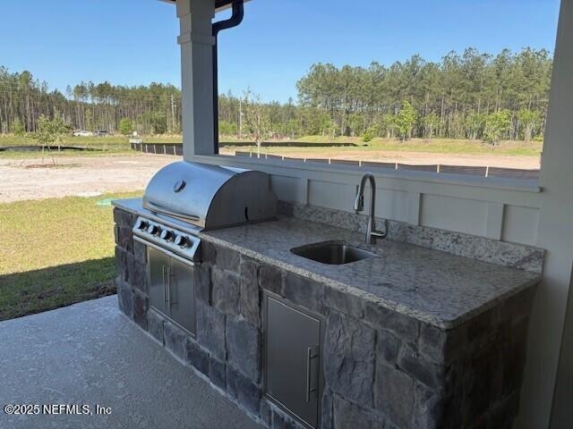 view of patio featuring exterior kitchen, a sink, a wooded view, and area for grilling