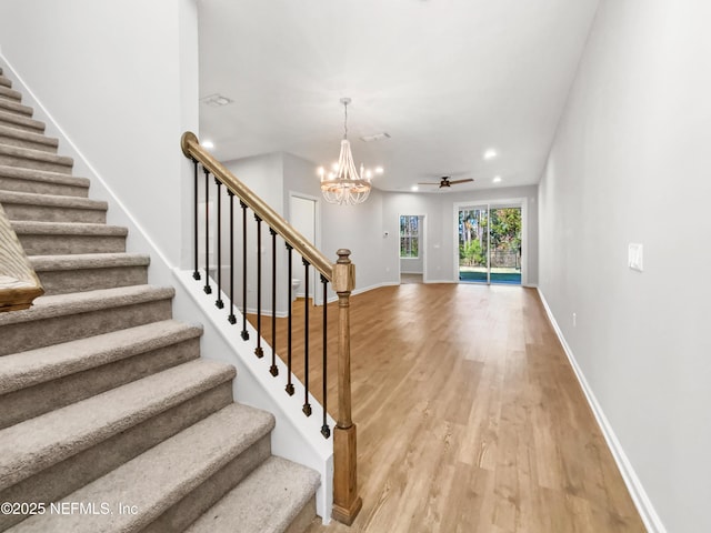 staircase featuring ceiling fan with notable chandelier and hardwood / wood-style flooring