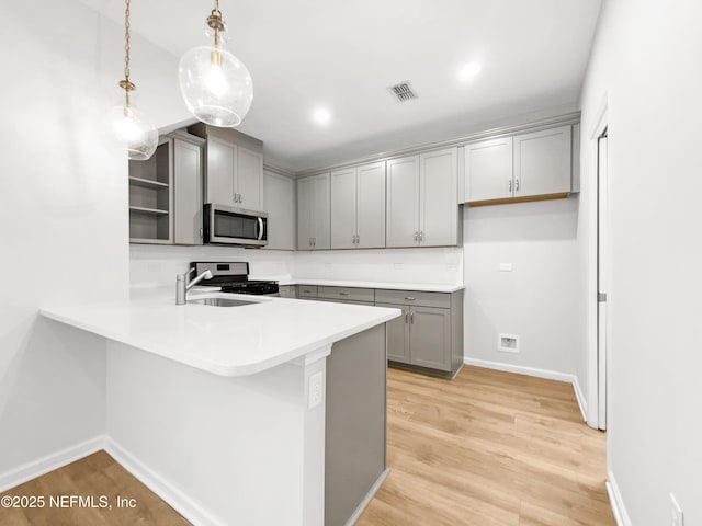 kitchen with stainless steel appliances, sink, light hardwood / wood-style flooring, kitchen peninsula, and pendant lighting