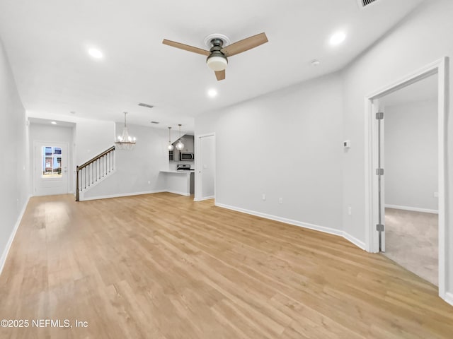 unfurnished living room featuring ceiling fan with notable chandelier and light hardwood / wood-style floors