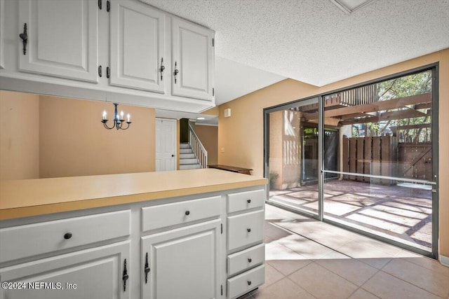 kitchen with a notable chandelier, a textured ceiling, light tile flooring, and white cabinetry