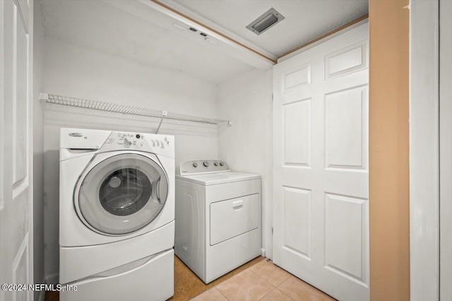 clothes washing area featuring washer and clothes dryer and light tile floors