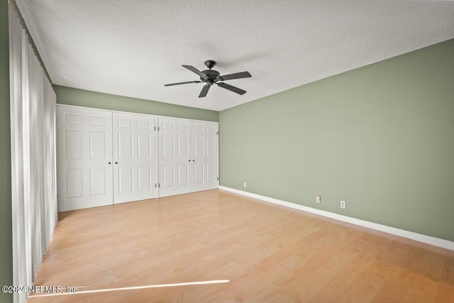 unfurnished bedroom with two closets, ceiling fan, a textured ceiling, and light wood-type flooring