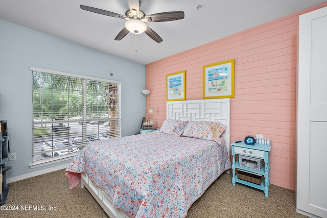 carpeted bedroom with ceiling fan and wood walls