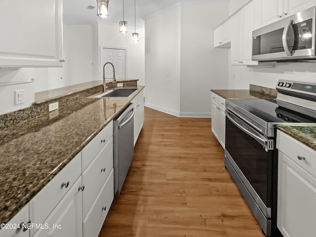 kitchen featuring dark stone counters, stainless steel appliances, white cabinets, light hardwood / wood-style floors, and hanging light fixtures