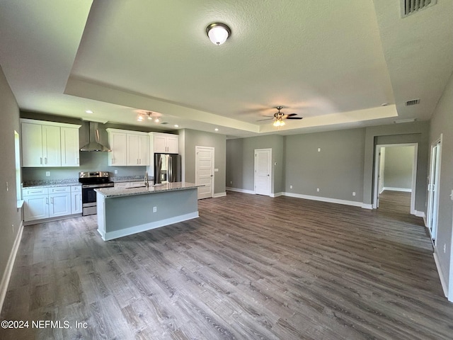 kitchen featuring stainless steel appliances, white cabinets, a raised ceiling, and wall chimney range hood