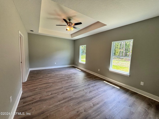 spare room featuring a textured ceiling, dark wood-type flooring, a tray ceiling, and ceiling fan