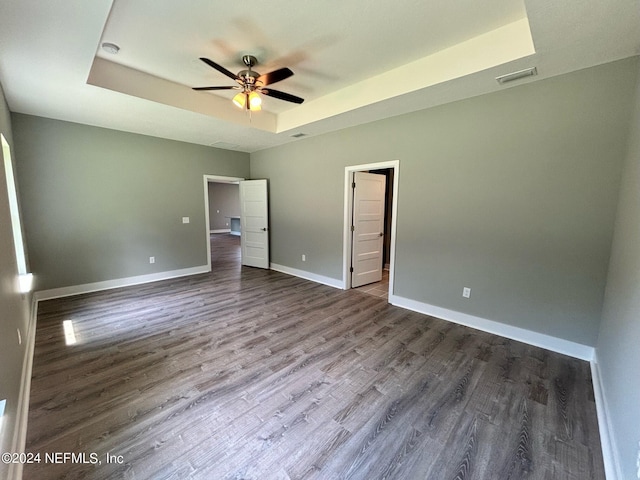 unfurnished bedroom with a spacious closet, ceiling fan, hardwood / wood-style floors, and a tray ceiling