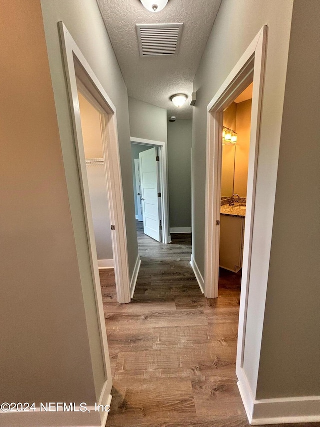 corridor with a textured ceiling and hardwood / wood-style floors