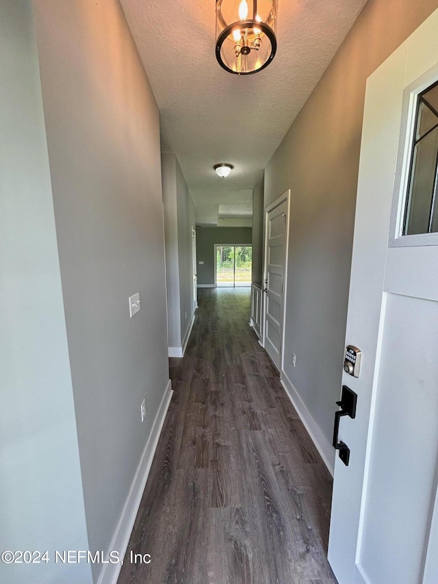 hallway with a textured ceiling, an inviting chandelier, and dark hardwood / wood-style flooring