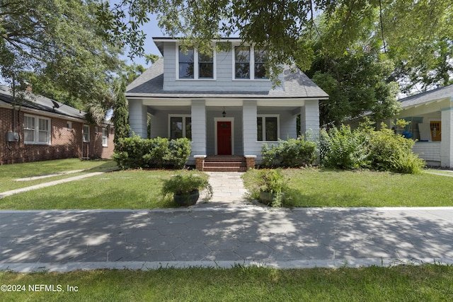 bungalow with a front yard, covered porch, and roof with shingles