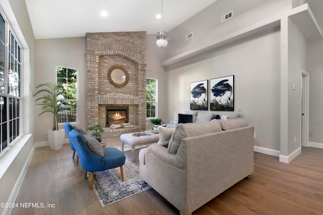 living room featuring a brick fireplace, light hardwood / wood-style floors, high vaulted ceiling, and a wealth of natural light