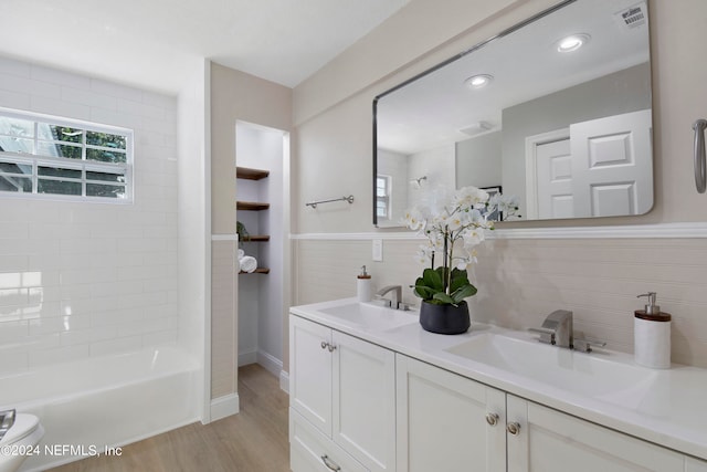 bathroom featuring wood-type flooring, vanity, tiled shower / bath combo, and tile walls