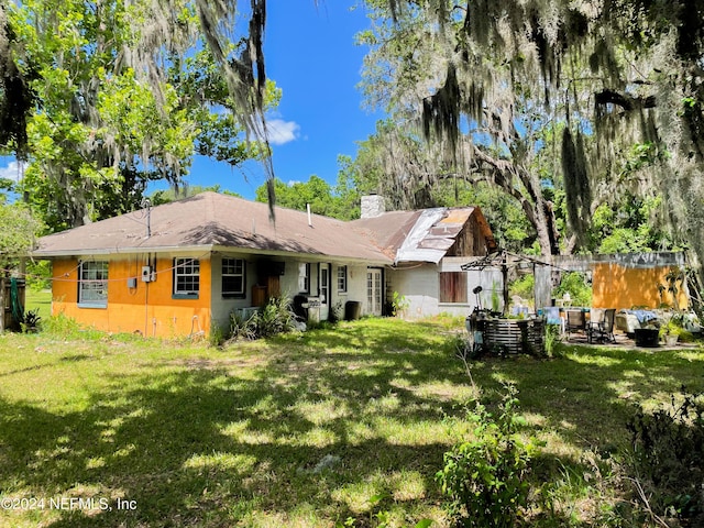 rear view of property featuring a chimney and a yard