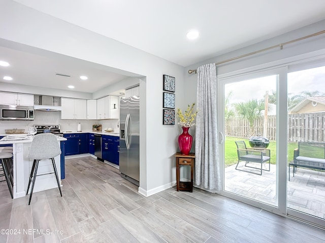 kitchen featuring a breakfast bar, blue cabinets, appliances with stainless steel finishes, light hardwood / wood-style floors, and white cabinetry