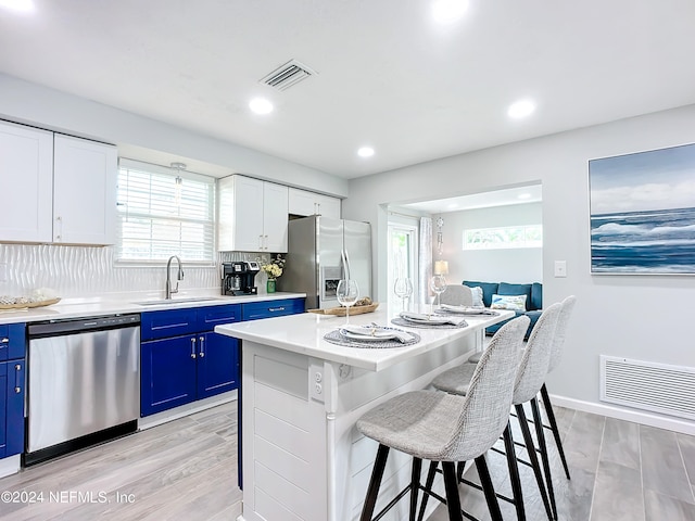 kitchen featuring stainless steel appliances, sink, blue cabinetry, a center island, and white cabinetry