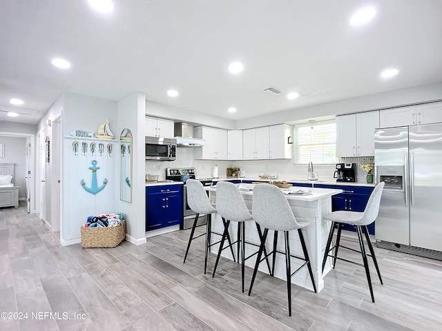 kitchen featuring a center island, white cabinets, blue cabinets, appliances with stainless steel finishes, and a breakfast bar area