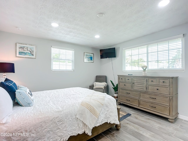 bedroom with light wood-type flooring, a textured ceiling, and multiple windows