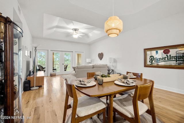 dining area with ceiling fan, a raised ceiling, a barn door, light wood-type flooring, and french doors