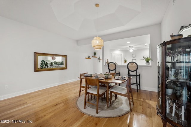 dining space featuring ceiling fan, light wood-type flooring, and a raised ceiling