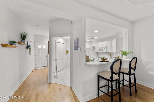 kitchen featuring a kitchen bar, white appliances, white cabinetry, and light wood-type flooring