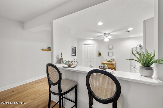 kitchen featuring a kitchen breakfast bar, ceiling fan, light hardwood / wood-style floors, and kitchen peninsula