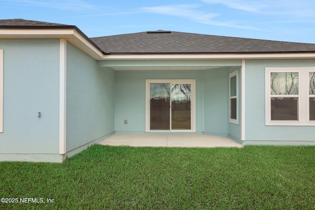 rear view of property featuring a shingled roof, stucco siding, a yard, and a patio