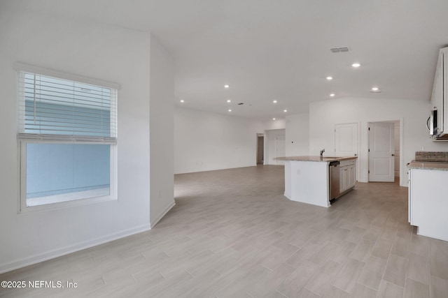 kitchen featuring stainless steel appliances, a sink, visible vents, open floor plan, and a center island with sink