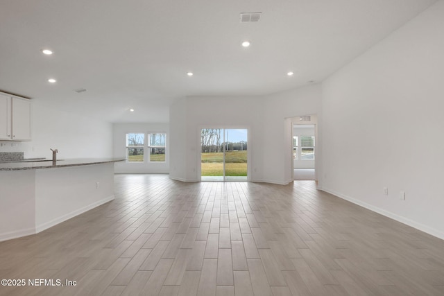 unfurnished living room featuring light wood-type flooring, baseboards, visible vents, and recessed lighting