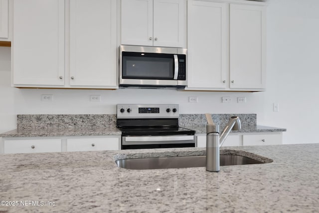 kitchen featuring stainless steel appliances, light stone counters, a sink, and white cabinetry