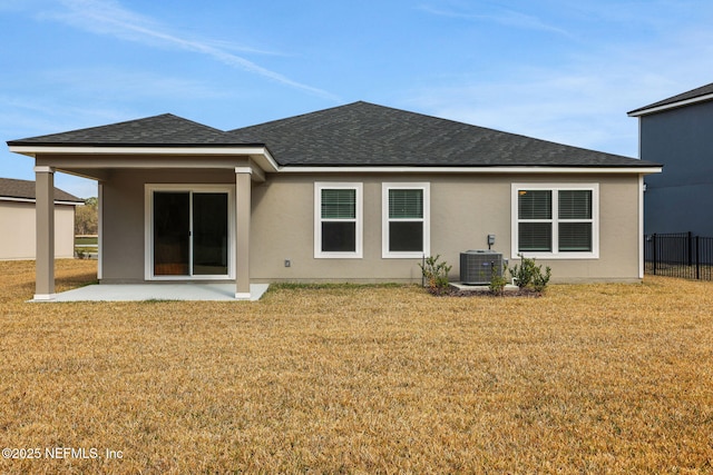 rear view of property featuring central AC unit, a lawn, roof with shingles, and fence