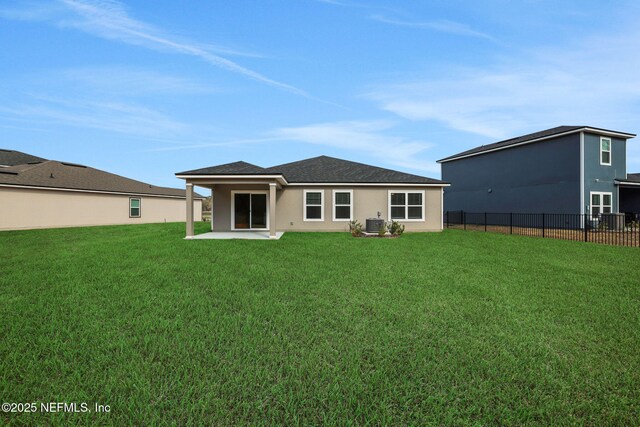 rear view of property with stucco siding, a lawn, fence, roof with shingles, and a patio area