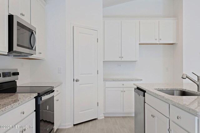 kitchen with wood tiled floor, light stone counters, appliances with stainless steel finishes, white cabinets, and a sink