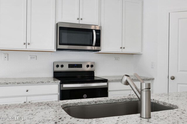 kitchen with light stone counters, appliances with stainless steel finishes, white cabinetry, and a sink