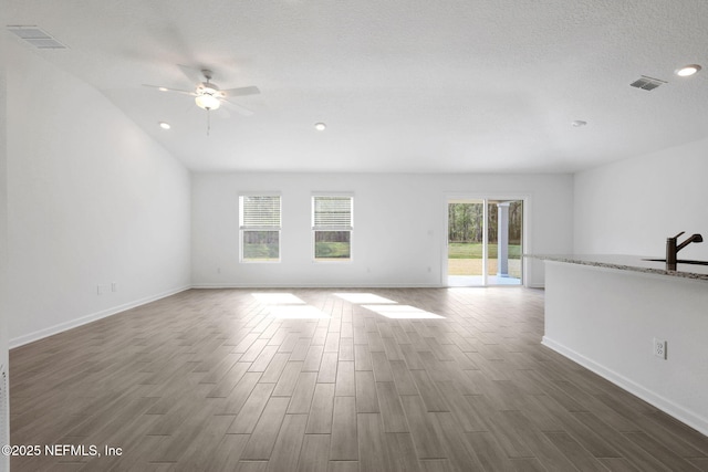 unfurnished living room with visible vents, baseboards, a textured ceiling, and dark wood-style floors