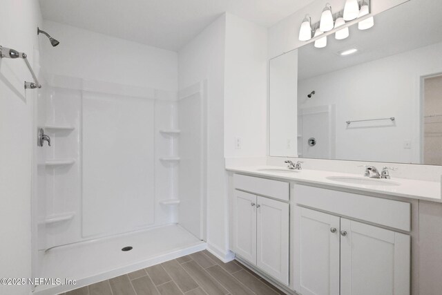 full bathroom with double vanity, wood finish floors, walk in shower, and a sink