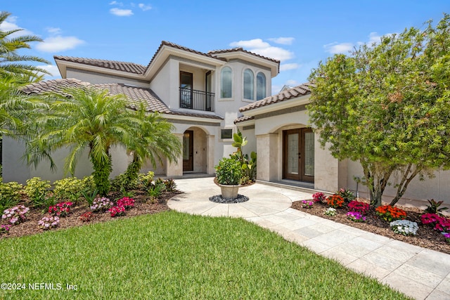 mediterranean / spanish-style home featuring a balcony, a front yard, and french doors