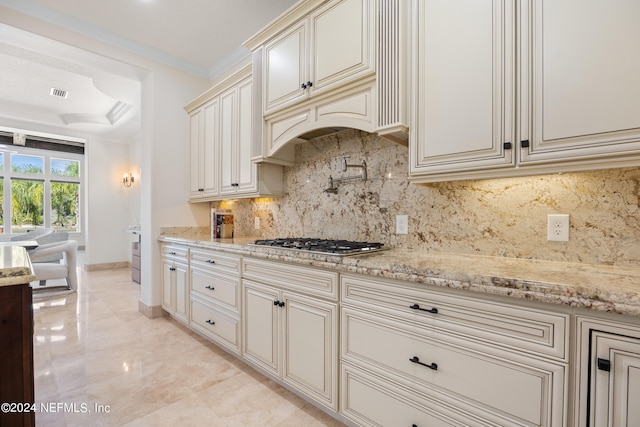 kitchen with decorative backsplash, crown molding, stainless steel gas cooktop, light stone countertops, and cream cabinetry