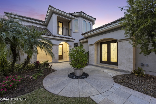 exterior entry at dusk with french doors and a balcony