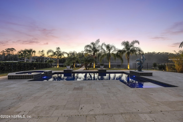 pool at dusk with a patio and an in ground hot tub