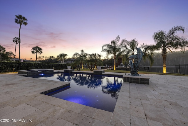 pool at dusk with an in ground hot tub and a patio