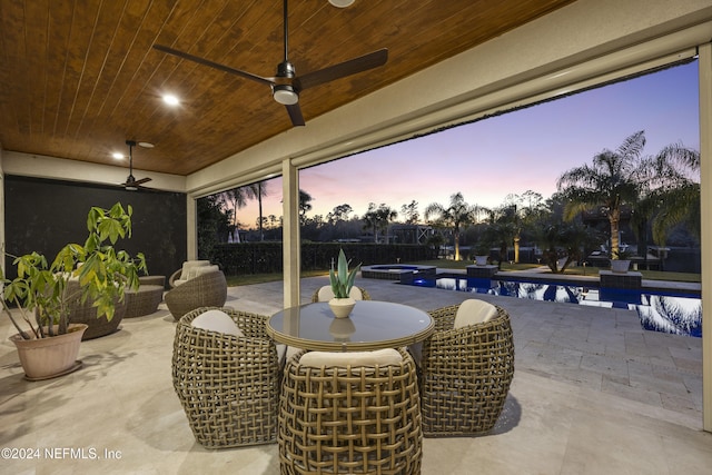 patio terrace at dusk featuring ceiling fan and a fenced in pool