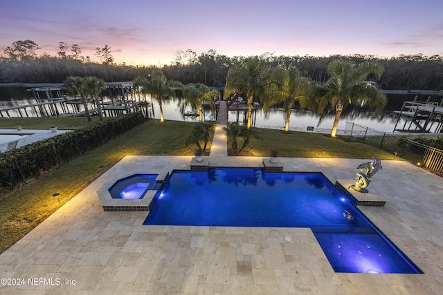 pool at dusk with a water view, a lawn, a patio area, and an in ground hot tub