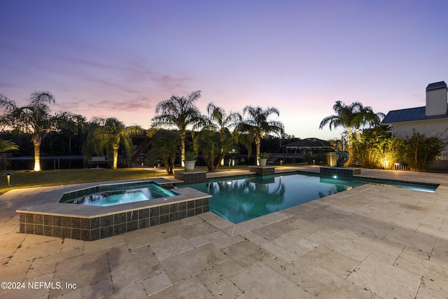 pool at dusk featuring an in ground hot tub and a patio area