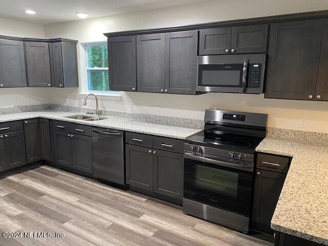 kitchen with appliances with stainless steel finishes, sink, light stone counters, and light wood-type flooring