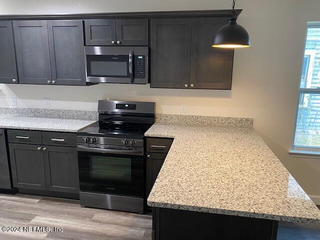 kitchen featuring light stone counters, stainless steel appliances, decorative light fixtures, and a wealth of natural light