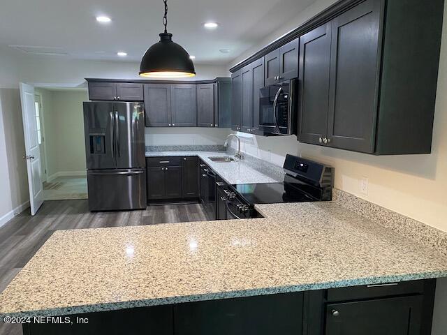 kitchen with black electric range oven, sink, light stone counters, decorative light fixtures, and stainless steel fridge