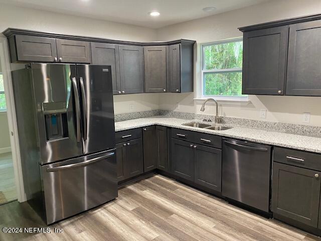 kitchen featuring dishwasher, sink, stainless steel fridge, light stone countertops, and light wood-type flooring