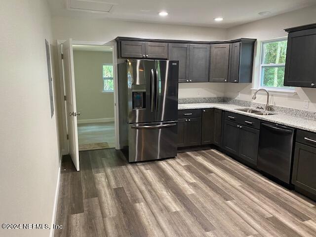 kitchen featuring dishwasher, sink, light stone counters, stainless steel fridge with ice dispenser, and light wood-type flooring