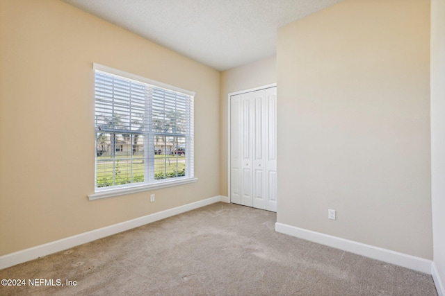 unfurnished bedroom with light carpet, a textured ceiling, and a closet